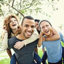 Friends giving piggyback rides and laughing together in the park.