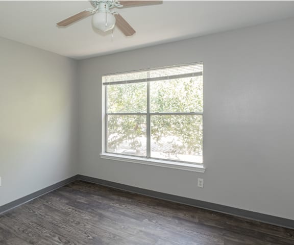 an empty bedroom with a large window and wood flooring