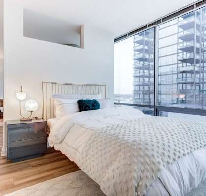 A bedroom with a large bed and a view of a building outside the window.