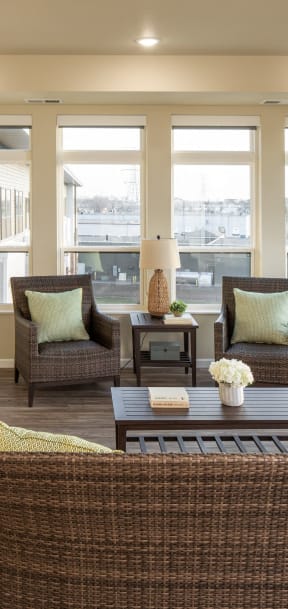 a living room with wicker chairs and a table and windows