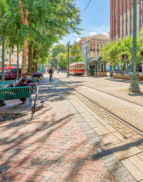 a city street with streetcar tracks and people sitting on benches