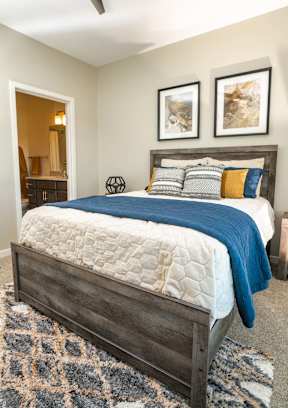 A bed with a blue blanket and pillows is in the foreground of a room.