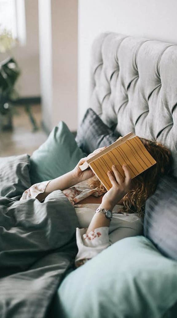 a woman laying on a couch reading a book