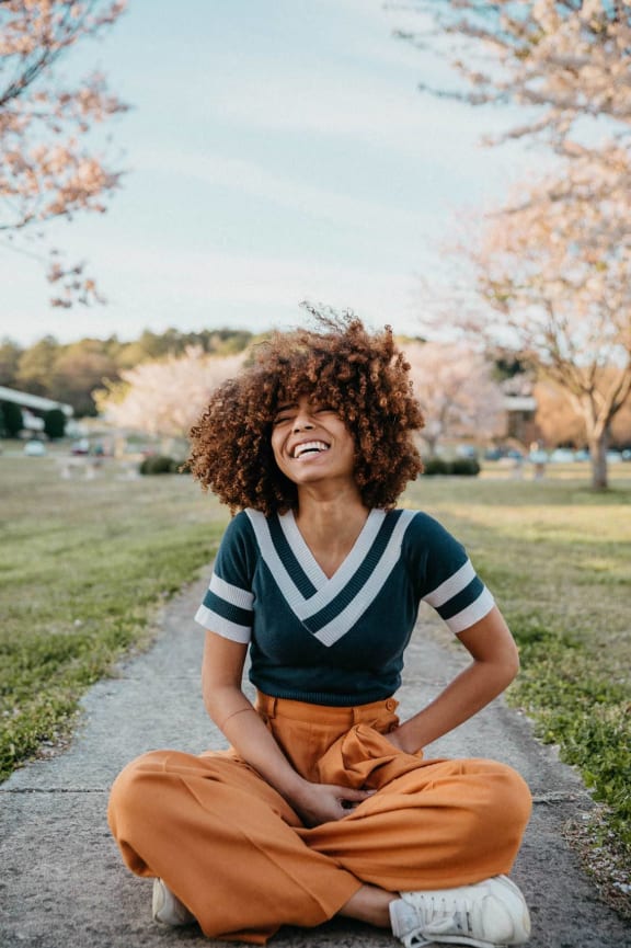 a woman laughing while sitting on a sidewalk