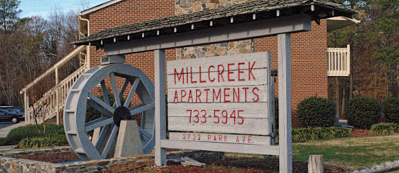 a sign for mill creek apartments with a water wheel