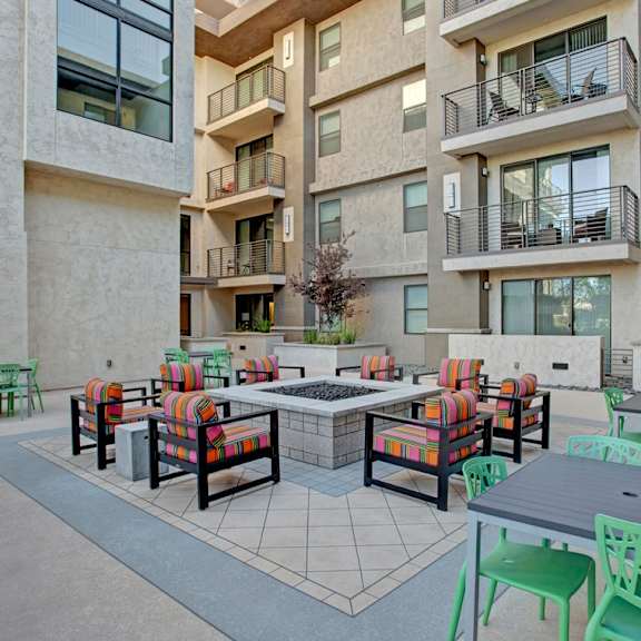 An outdoor patio surrounded by chairs with colorful cushions and with tables and chairs around them at Escape Apartments. 