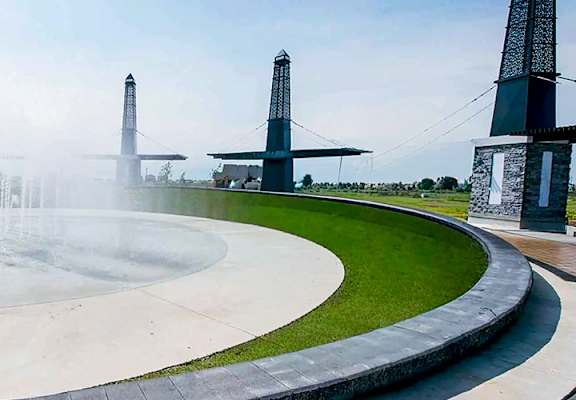 A fountain in the middle of a circular walkway with four tall structures in the background.