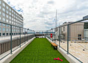 Thumbnail 6 of 6 - A rooftop patio with a green lawn and a metal fence.