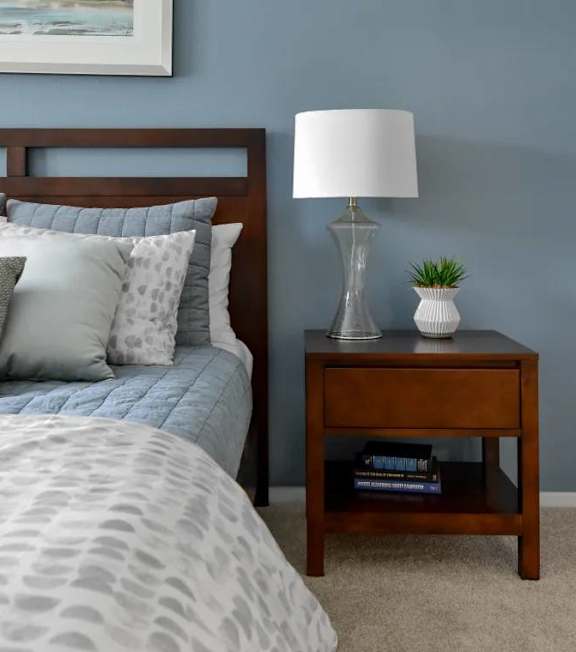 A bedroom with a bed, nightstand, and lamp.