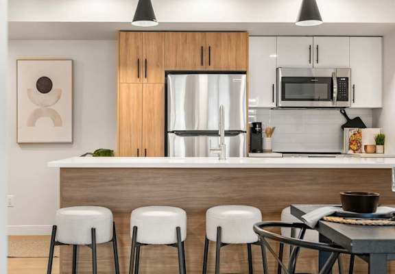 A modern kitchen with a wooden island and white stools.at Skyway Apartments, Calgary, AB T3B 5V6