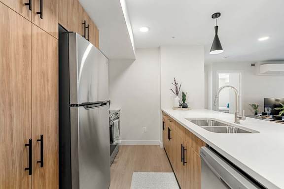 A modern kitchen with a stainless steel refrigerator and wooden cabinets.at Skyway Apartments, Calgary, AB T3B 5V6