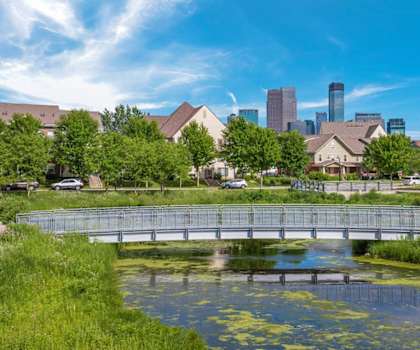 A bridge over a pond with a city skyline in the background.