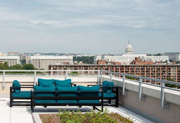 A bench with green cushions is on a balcony overlooking a cityscape.