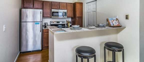 A kitchen with a refrigerator, microwave, oven, and two stools.