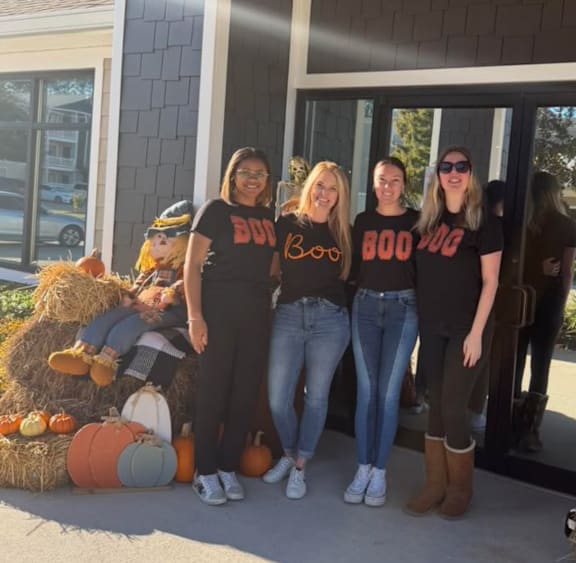 Four women wearing BOO shirts stand in front of a building.