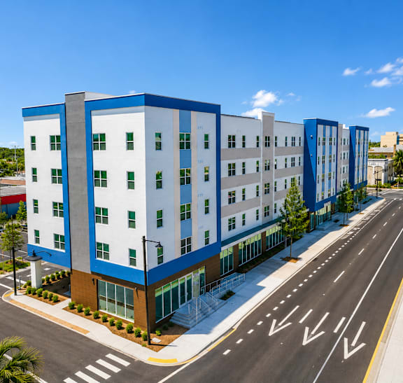 A modern multi-story building with blue and white exterior and a parking lot in front.