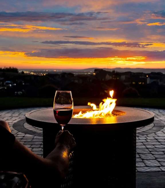 A person is holding a glass of wine in front of a fire pit.