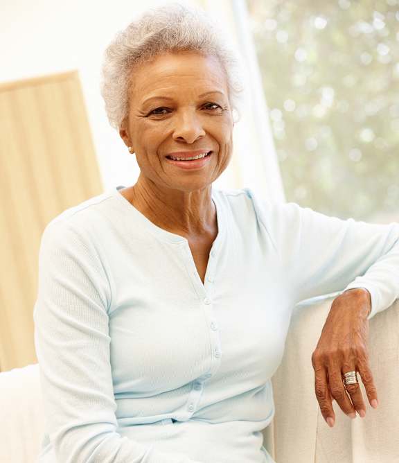 An older woman with a ring on her finger is sitting on a white couch.
