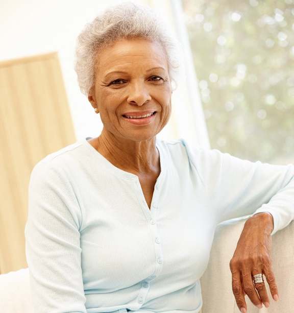 An older woman with a ring on her finger is sitting on a white couch.