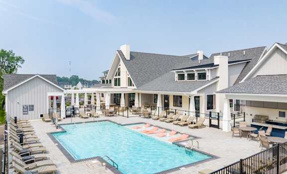 A large outdoor swimming pool surrounded by sun loungers and a building with a white exterior.