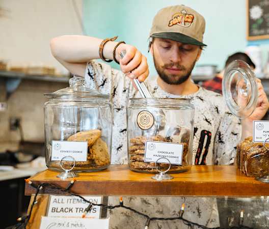a man behind a counter with jars of bread and other baked goods at The Hemlock, Seattle, WA