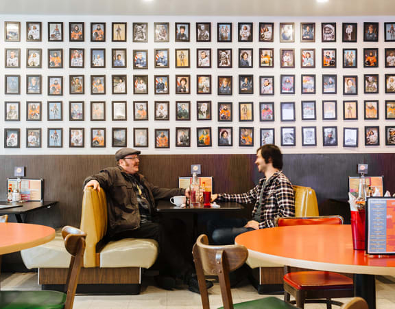 people sitting at a table in front of a wall of framed photos