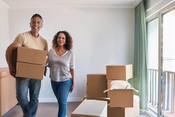 A woman is holding a potted plant and a man is carrying a cardboard box.