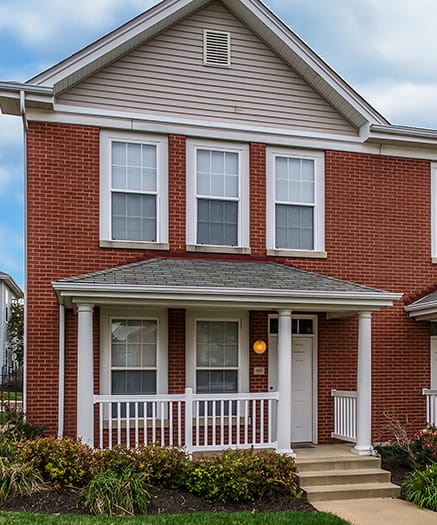 a red brick townhome with a porch and a sidewalk in front of it at Renaissance Place at Grand Apartments