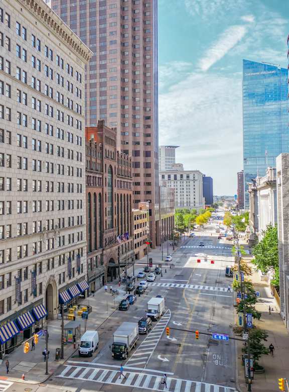 A city street with a mix of modern and older buildings, cars on the road, and a clear sky.