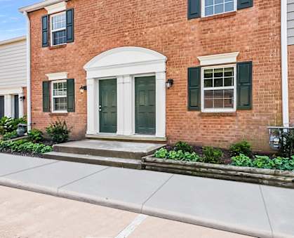 the front of a brick building with green shutters and a white door