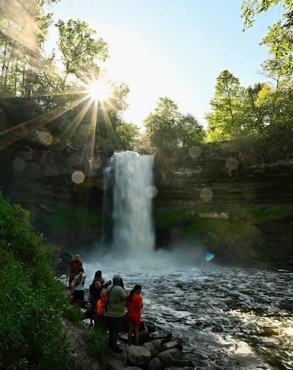A group of people are standing in front of a waterfall.