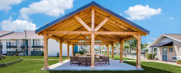 a wooden pavilion with a table and chairs on a lawn