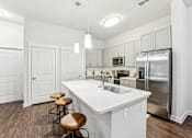 Thumbnail 24 of 31 - A white kitchen with a refrigerator, sink, and bar stools.