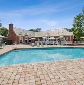 A large outdoor swimming pool with a brick patio and a house in the background.