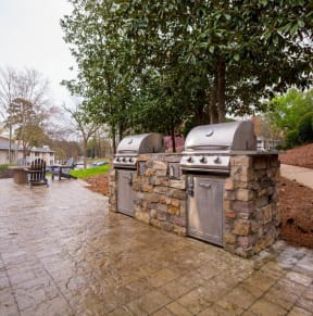 a stone outdoor kitchen with two grills and two umbrellas