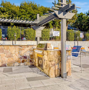 a picnic area with a grill and chairs and a stone wall at Edgemont Apartments, PRG Real Estate, Greenville, 29615