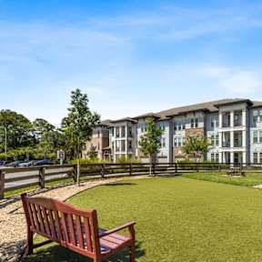A grassy area in front of apartment buildings with a bench and a tree.