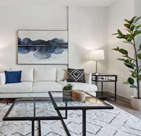 A modern living room with a white sofa, a grey ottoman, and a large abstract painting on the wall.