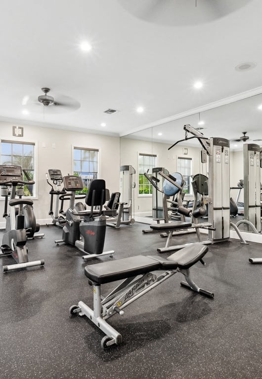 a gym with cardio equipment and weights in a building with windows