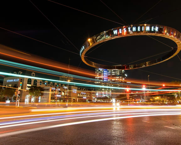 a city at night with streaks of traffic and a lit up arch in the middle of the