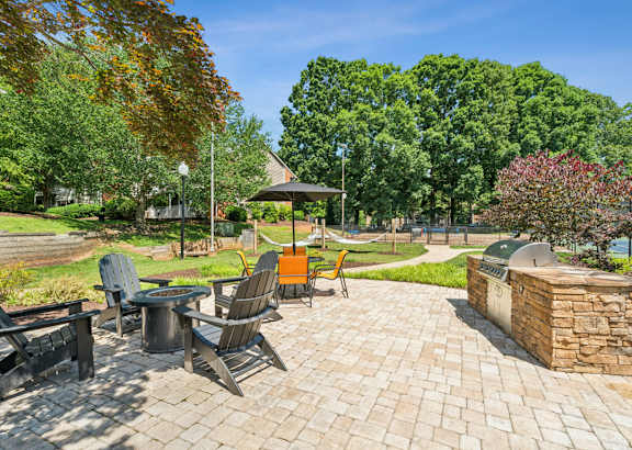 A patio with chairs and a table is surrounded by trees. at Woodcreek Apartments, North Carolina
