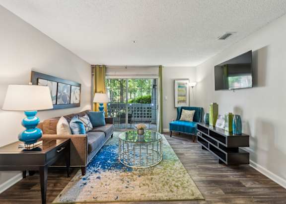 A living room with a blue rug and a glass table.