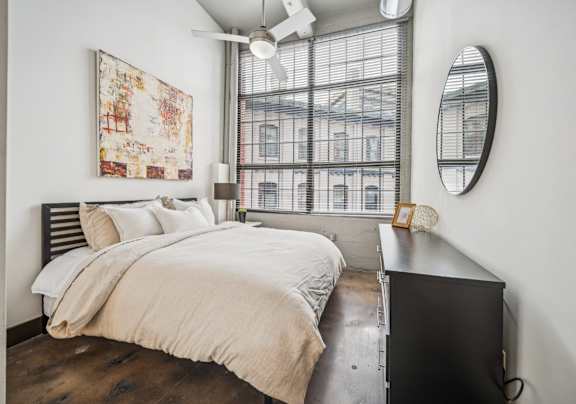 A bedroom with a large bed and a window with blinds.