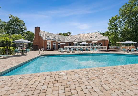 A large outdoor swimming pool with a brick patio and a house in the background.