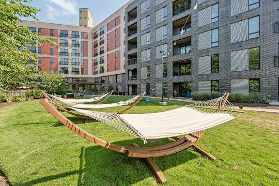 A hammock is set up in a grassy area in front of apartment buildings.