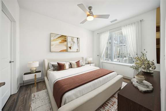 A bedroom with a bed, a ceiling fan, and a painting on the wall.