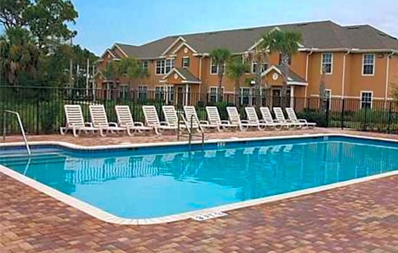 a large pool with white chairs in front of an apartment building