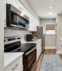 A kitchen with white cabinets and black appliances. at The Courtyards of Chanticleer, Virginia Beach, VA