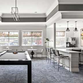 A pool table is in the middle of a room with a bar and chairs.