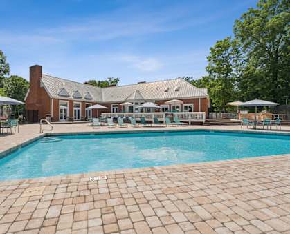 A large outdoor swimming pool with a brick patio and a house in the background. at The Timbers Apartments, Richmond, VA, 23235